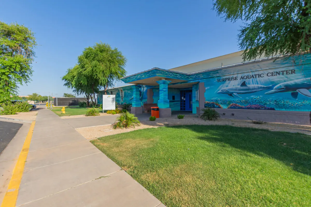 A vibrant mural featuring playful dolphins is painted on the entrance area of an aquatic facility. The foreground shows a well-manicured lawn and a clear pathway leading up to the building, invoking a sense of community and family-friendly fun.