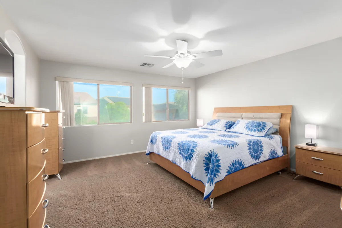 A tranquil bedroom with a bed covered in a blue patterned quilt, large windows letting in natural light, and a dresser with a mirror. The room feels airy, peaceful, and inviting, ideal for unwinding.