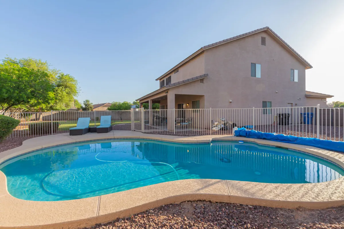 A sparkling swimming pool surrounded by inviting lounge chairs and a cozy back porch, all bathed in warm sunlight. The setting is perfect for relaxing after a day out at a game.