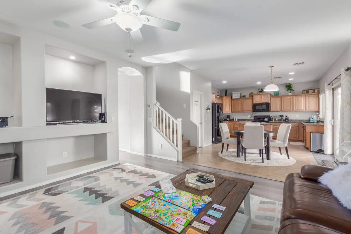 The image captures a cozy social scene with a coffee table set up for a board game, a comfortable couch, and a kitchen area visible in the background. The open layout provides a sense of seamless flow between living and kitchen spaces, ideal for entertaining and shared activities.
