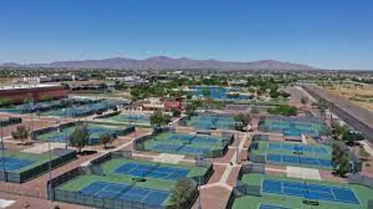 The image showcases well-maintained tennis courts set against a backdrop of desert mountains and palm-studded landscapes, with nearby community buildings enhancing the sense of a vibrant, social atmosphere. People can be seen playing tennis and gathering around the courts, adding energy and a communal vibe to the scene.