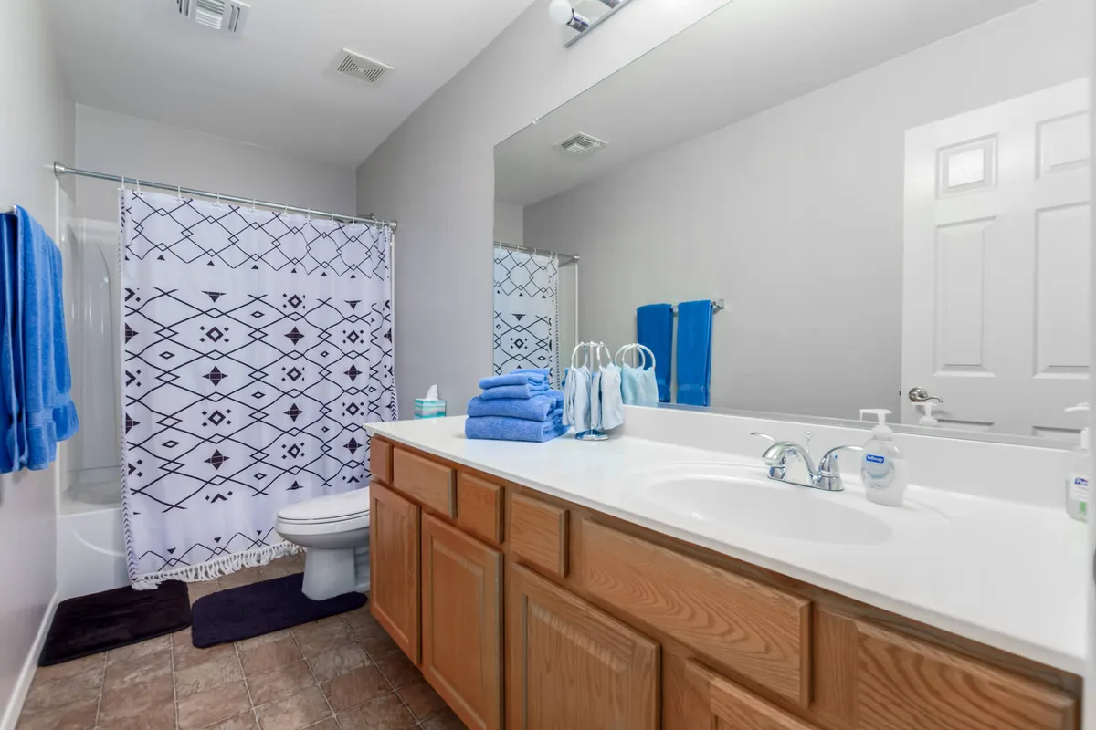 A refreshing bathroom scene with a vanity and sink, a shower featuring a patterned curtain, and neatly stacked towels. The space feels inviting, clean, and perfect for personal care routines.