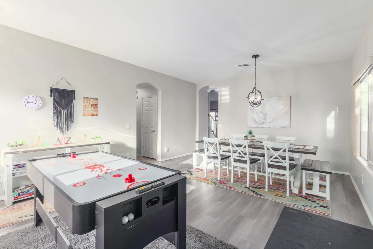A lively open-concept space showing a dining table set against a backdrop of decorative wall art and a striking light fixture. An air hockey table is nearby, hinting at a space meant for both dining and entertaining. The mood is cheerful, reflecting family fun and togetherness.
