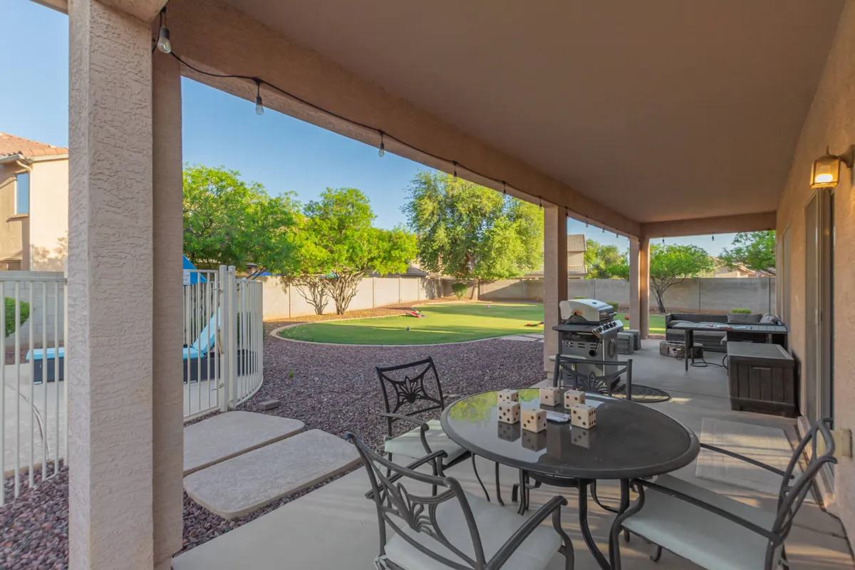 An inviting outdoor dining area with a grill and table set on a lush lawn, surrounded by trees. The scene suggests family barbecues, relaxed dinners, and children playing in the yard, embodying a laid-back, homey vibe.