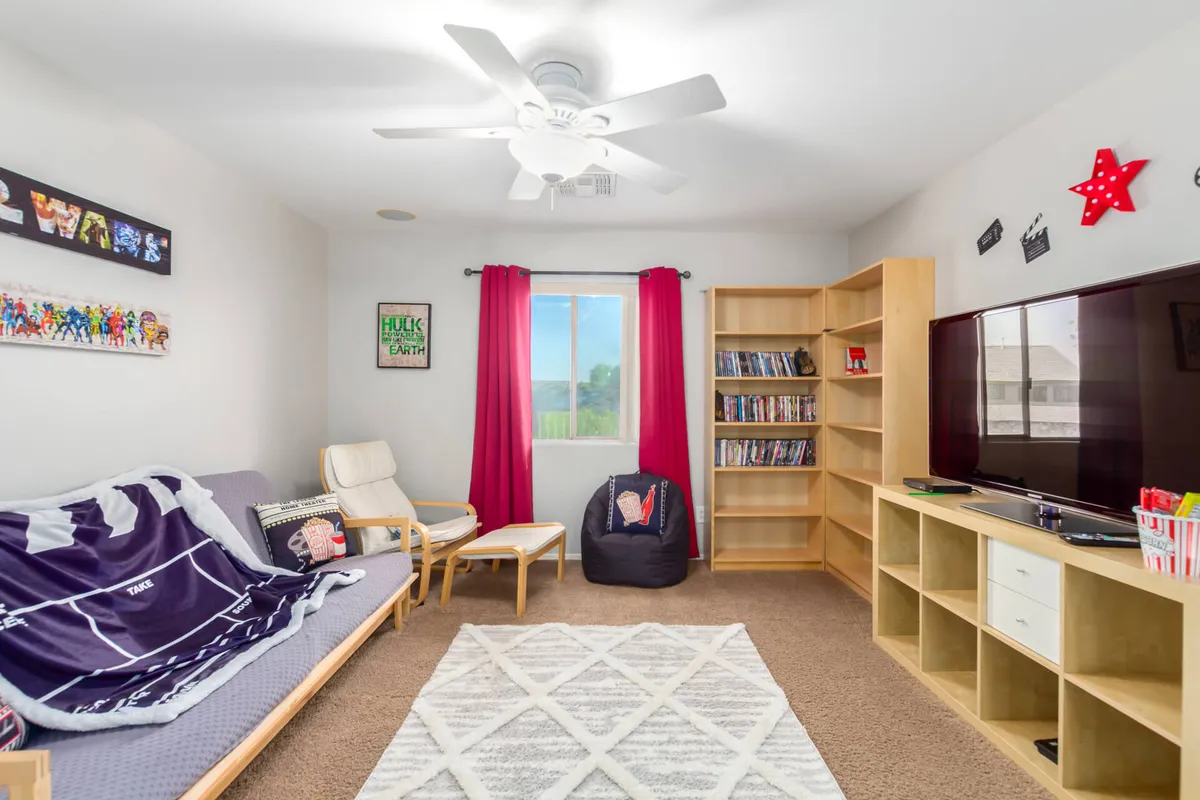 A bright living room scene with a sofa bed, bookshelf, television, and a large window allowing natural light to pour in. The setting feels casual and cheerful, inviting for reading, watching movies, or playing games.