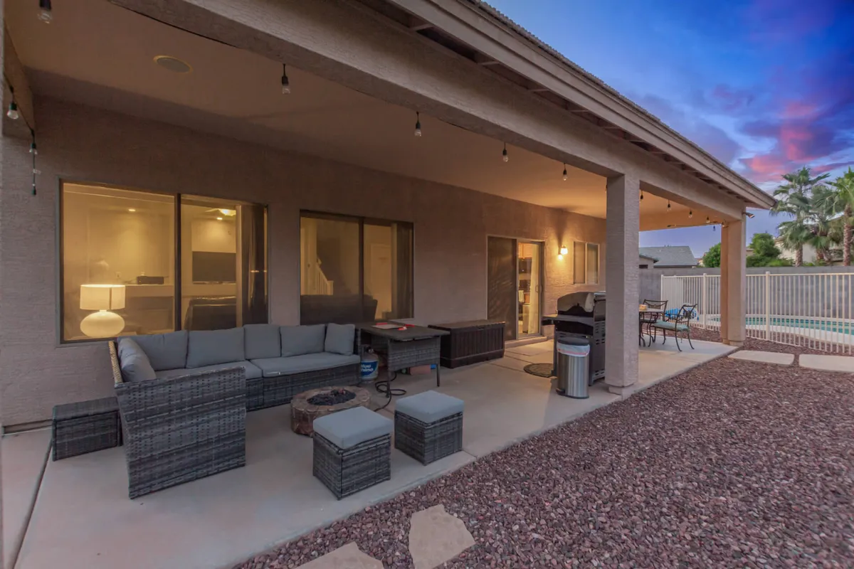 A cozy outdoor seating area with a fire pit overlooks the pool. String lights hang above, adding a touch of magic to the evening atmosphere. The scene feels perfect for al fresco dining, poolside relaxation, or stargazing with friends and family.