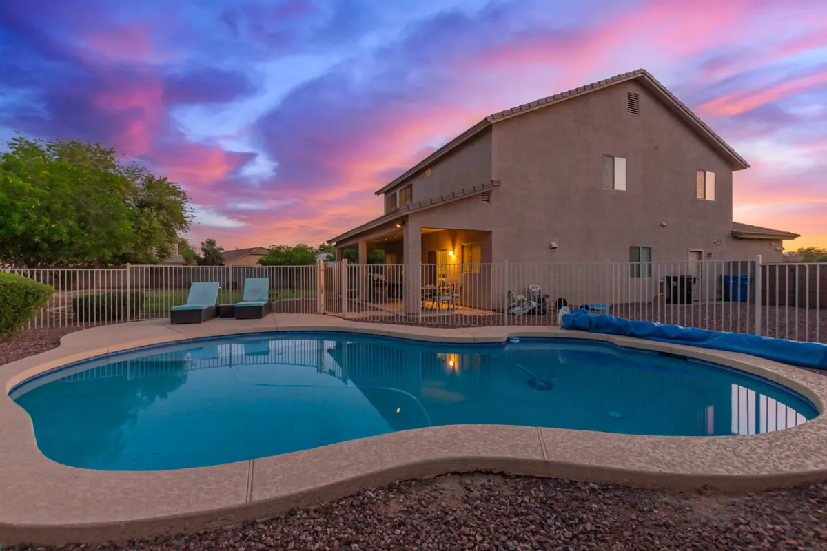 This image features a sparkling swimming pool bordered by lounge chairs and a view of the house set against a colorful Arizona sky. The scene is inviting, with the pool and patio area illuminated by soft evening light, evoking a sense of relaxation and outdoor enjoyment.