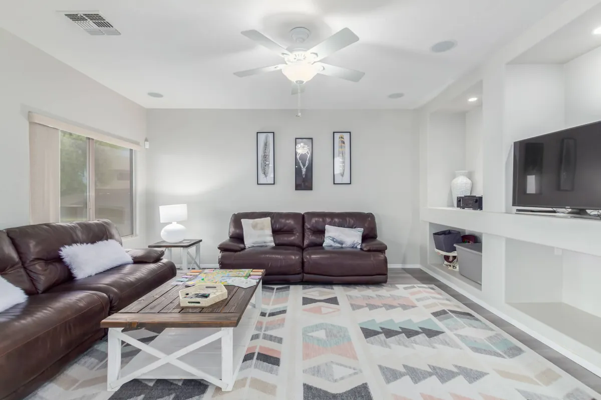 This image features a living area with brown leather sofas, a wooden coffee table, a colorful area rug, and artwork on the walls. The space radiates comfort and is clearly arranged for socializing and relaxation, offering ample natural light to highlight the warm desert tones and modern Southwestern decor.