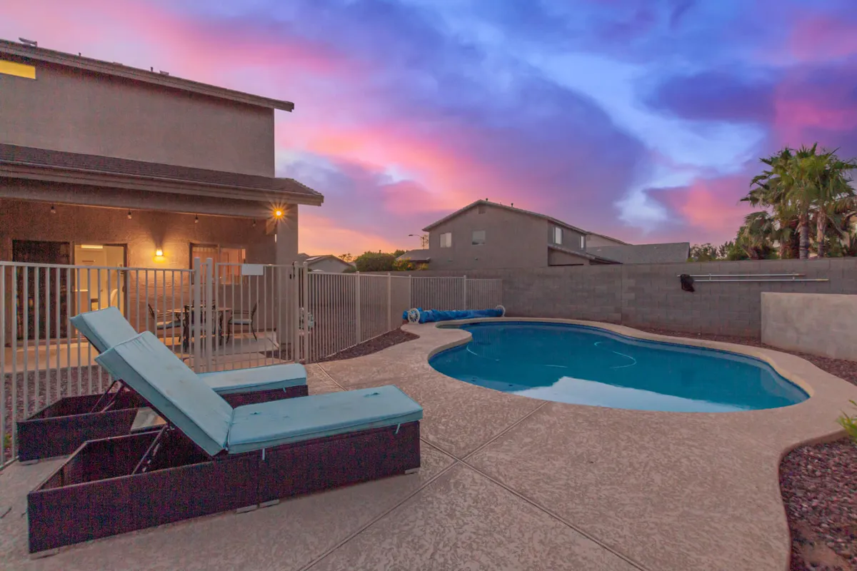 This image features a swimming pool surrounded by lounge chairs under a colorful sky, creating a relaxed and stylish outdoor atmosphere. The setting suggests a perfect space for sunbathing, socializing, and enjoying evening gatherings poolside.